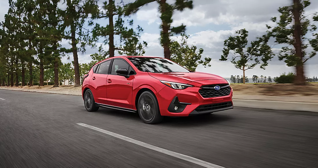 Red Subaru Impreza hatchback driving on a tree-lined road